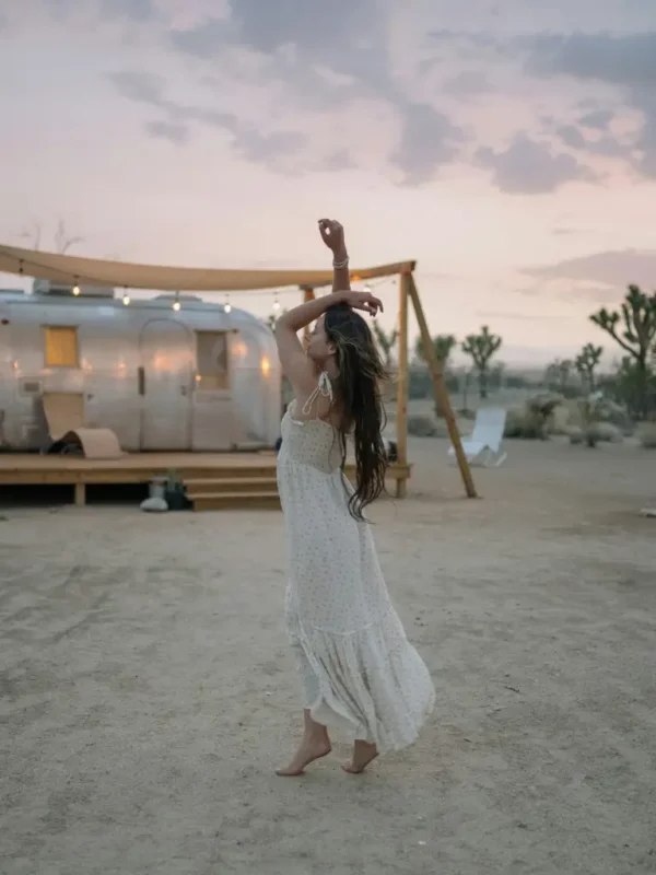 Petite woman wearing a flowing white boho maxi dress, lightweight fabric with delicate pattern, styled for outdoor summer wear.