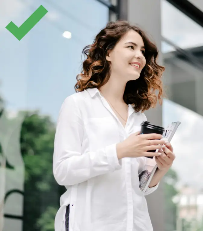 A petite woman wearing a flattering v-neck top while drinking coffee on the way to the office.