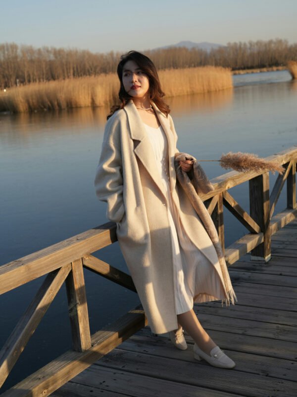 Petite woman wearing a long cream coat over a white dress