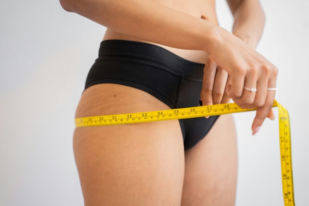 Woman measuring around the fullest part of her hips with a flexible yellow measuring tape to determine her clothing size.