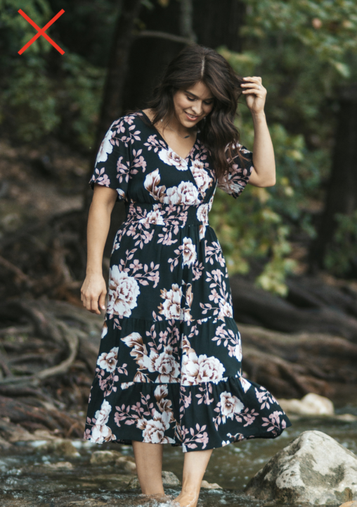Woman wearing a dark floral midi dress with oversized flower prints, illustrating a pattern that can overwhelm a petite frame.