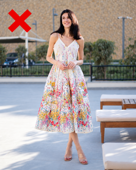 Woman wearing a colorful floral midi dress with a busy print and mid-calf hemline, marked with a red X as a less flattering petite dress option.